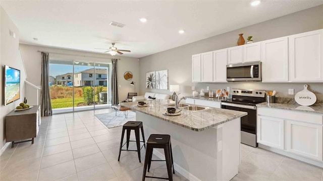 kitchen with white cabinets, stainless steel appliances, light stone countertops, and a kitchen island with sink