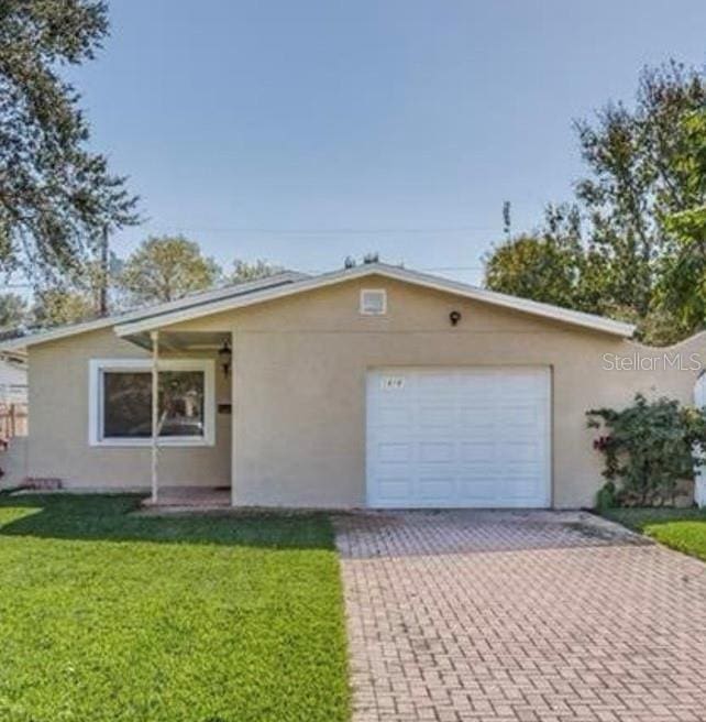 ranch-style house featuring an attached garage, a front lawn, stucco siding, and decorative driveway