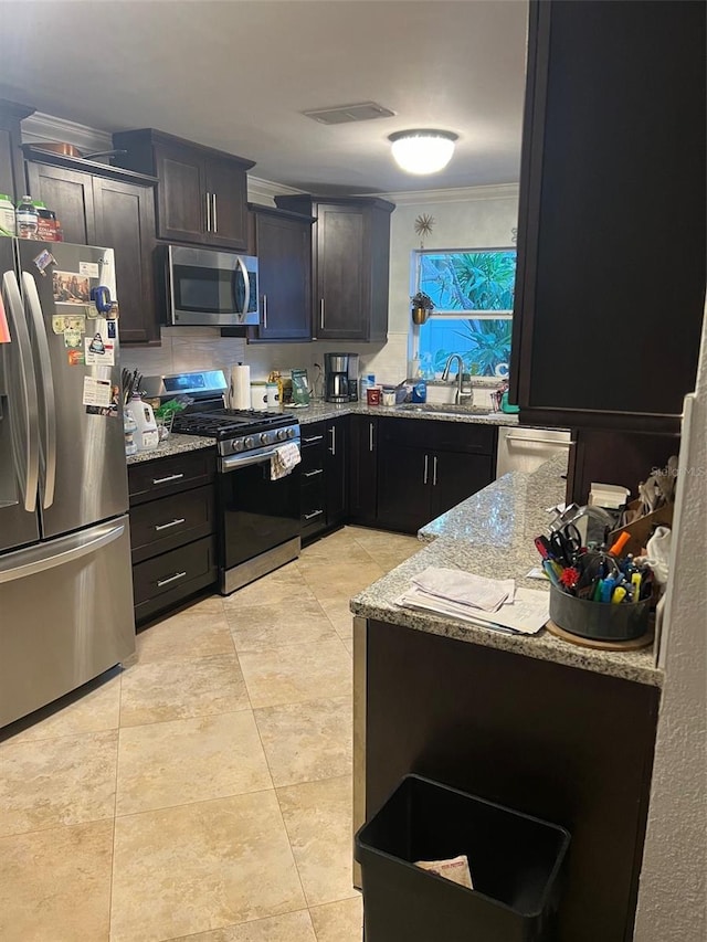 kitchen featuring sink, light stone counters, dark brown cabinets, ornamental molding, and stainless steel appliances