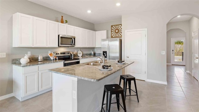 kitchen featuring sink, stainless steel appliances, white cabinets, light stone counters, and a center island with sink