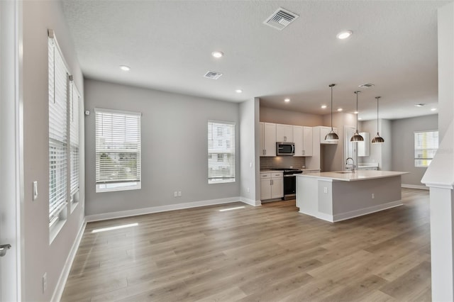 kitchen with white cabinetry, hanging light fixtures, light hardwood / wood-style flooring, a kitchen island with sink, and appliances with stainless steel finishes