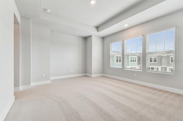 unfurnished room with a tray ceiling, light carpet, and a textured ceiling