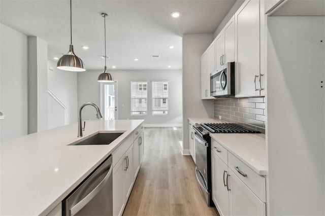 kitchen featuring white cabinetry, sink, stainless steel appliances, pendant lighting, and light wood-type flooring