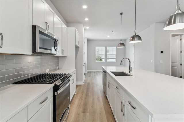 kitchen with sink, an island with sink, light hardwood / wood-style floors, decorative light fixtures, and appliances with stainless steel finishes