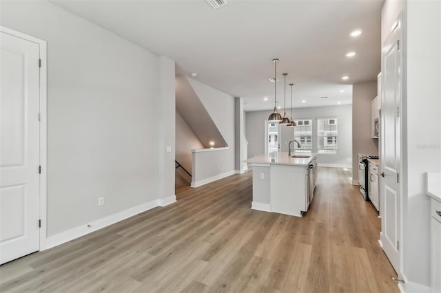 kitchen featuring light wood-type flooring, sink, a center island with sink, white cabinets, and hanging light fixtures