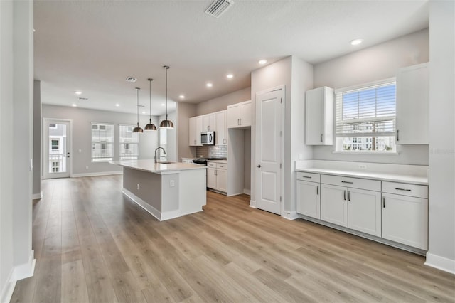 kitchen featuring sink, hanging light fixtures, a kitchen island with sink, white cabinets, and appliances with stainless steel finishes