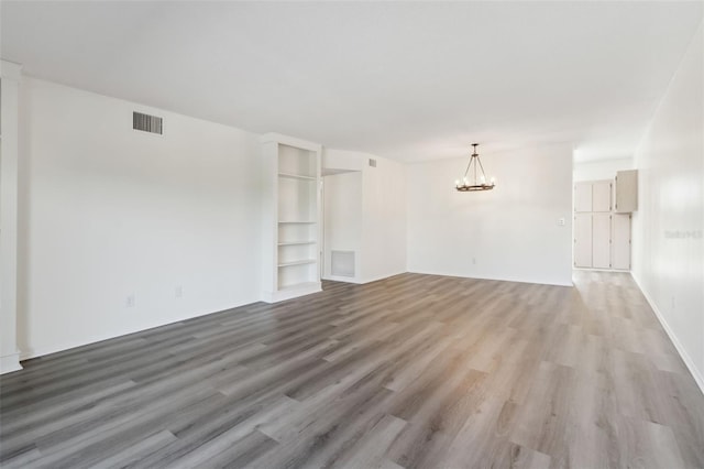 unfurnished living room with built in features, wood-type flooring, and an inviting chandelier