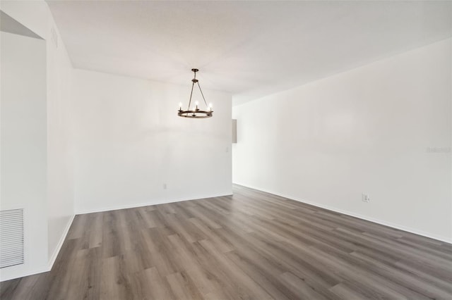 empty room featuring dark wood-type flooring and a chandelier