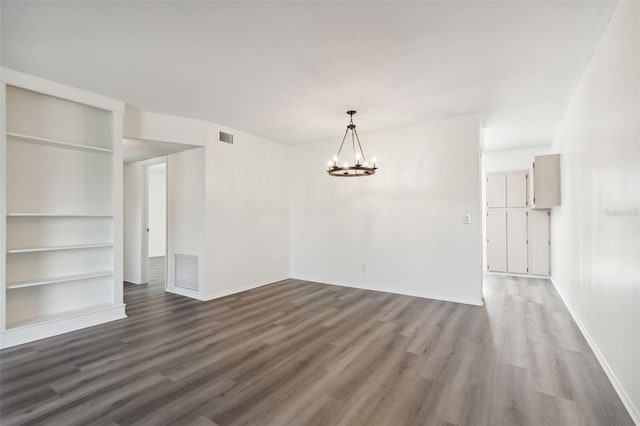 spare room featuring built in features, wood-type flooring, and an inviting chandelier