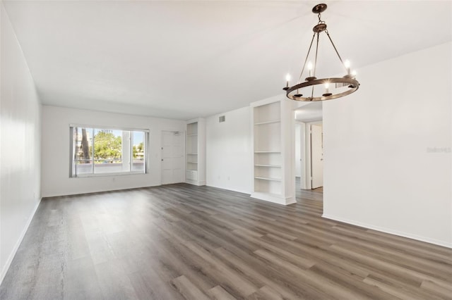 unfurnished living room featuring dark hardwood / wood-style flooring, an inviting chandelier, and built in shelves