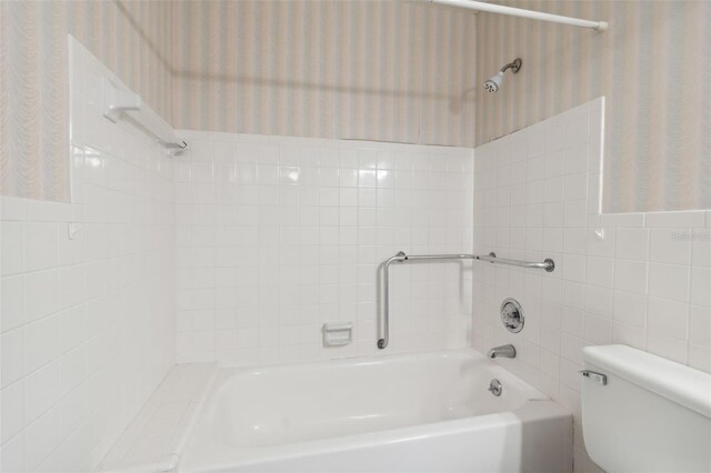 bathroom with toilet, tiled shower / bath combo, and tile walls