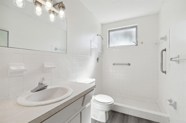 bathroom with a tile shower, wood-type flooring, tile walls, toilet, and vanity