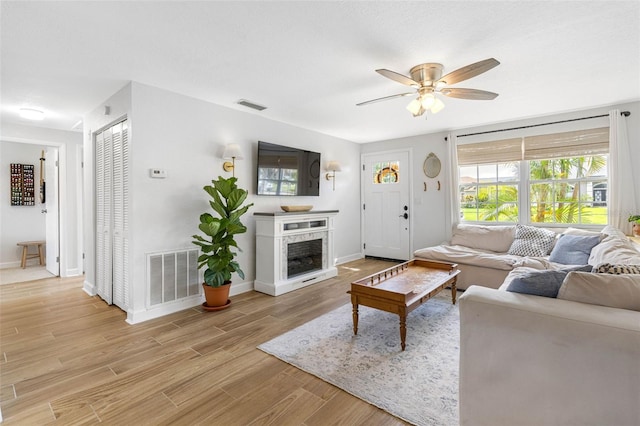 living area with light wood-type flooring, ceiling fan, a fireplace, and visible vents