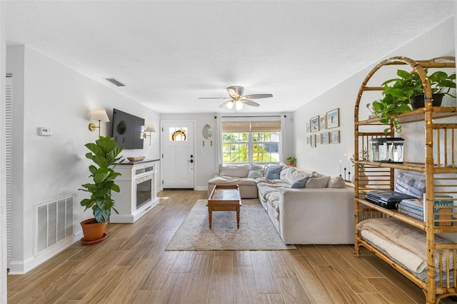 living area featuring visible vents, ceiling fan, baseboards, and wood finished floors