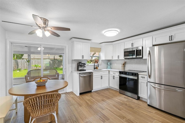 kitchen featuring stainless steel appliances, a sink, white cabinets, light countertops, and light wood-type flooring