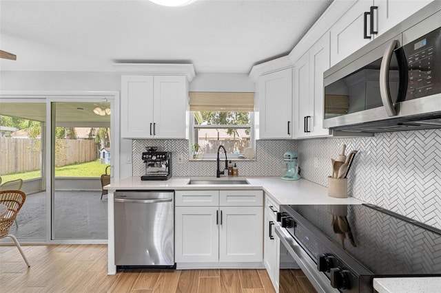 kitchen with tasteful backsplash, appliances with stainless steel finishes, light countertops, white cabinetry, and a sink