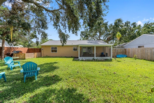 rear view of property featuring a sunroom, a fenced backyard, a lawn, and stucco siding