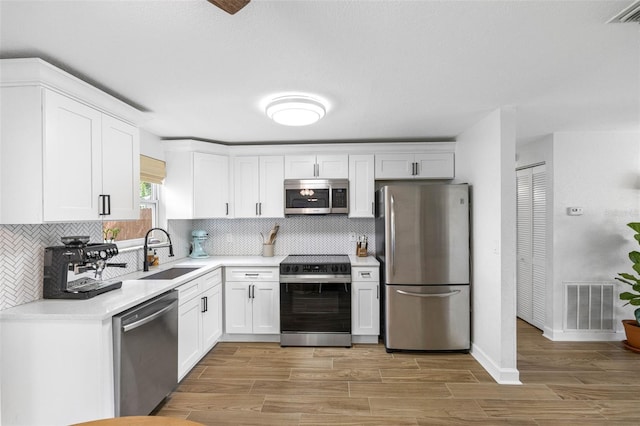 kitchen with a sink, visible vents, white cabinetry, light countertops, and appliances with stainless steel finishes