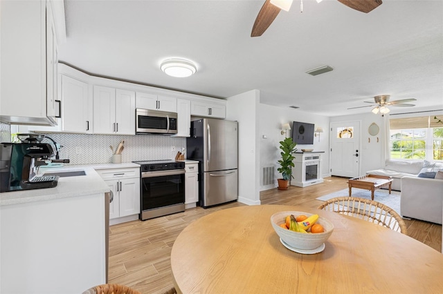 kitchen with stainless steel appliances, visible vents, white cabinets, open floor plan, and tasteful backsplash