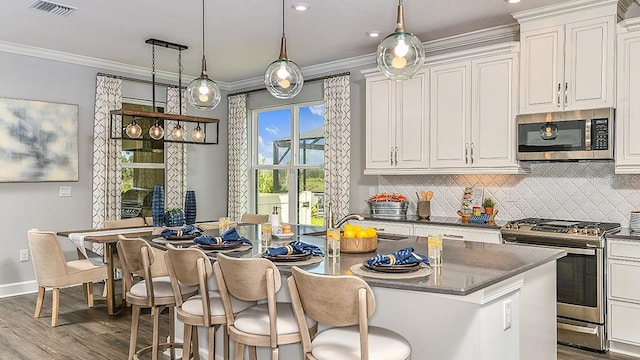 kitchen with white cabinets, decorative light fixtures, a kitchen island with sink, and appliances with stainless steel finishes