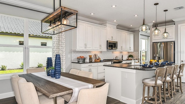 kitchen with hanging light fixtures, stainless steel appliances, dark hardwood / wood-style flooring, an island with sink, and white cabinets