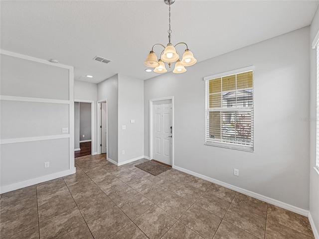 tiled spare room featuring an inviting chandelier