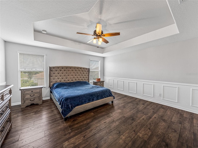 bedroom with dark hardwood / wood-style flooring, a textured ceiling, a tray ceiling, and ceiling fan