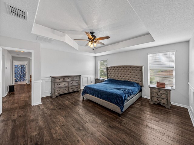 bedroom featuring multiple windows, dark hardwood / wood-style floors, a raised ceiling, and ceiling fan