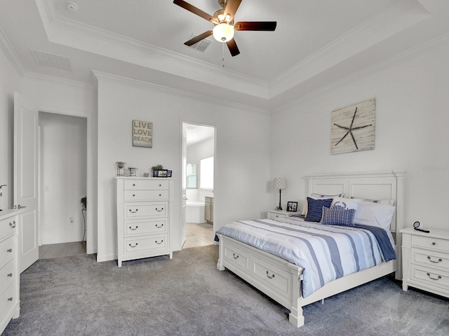 bedroom featuring ceiling fan, connected bathroom, a tray ceiling, crown molding, and light colored carpet