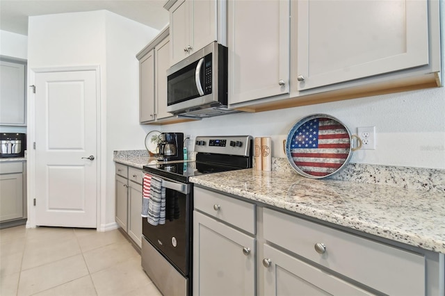 kitchen with appliances with stainless steel finishes, light stone counters, gray cabinets, and light tile patterned floors