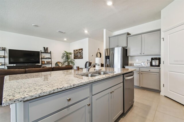 kitchen featuring a kitchen island with sink, gray cabinetry, stainless steel appliances, sink, and a textured ceiling