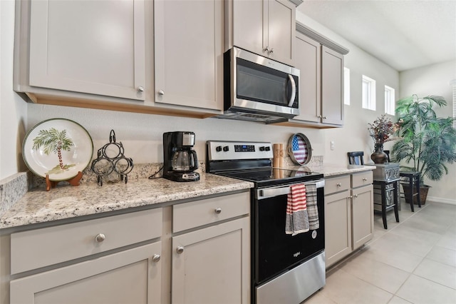 kitchen featuring gray cabinetry, light stone counters, stainless steel appliances, and light tile patterned flooring