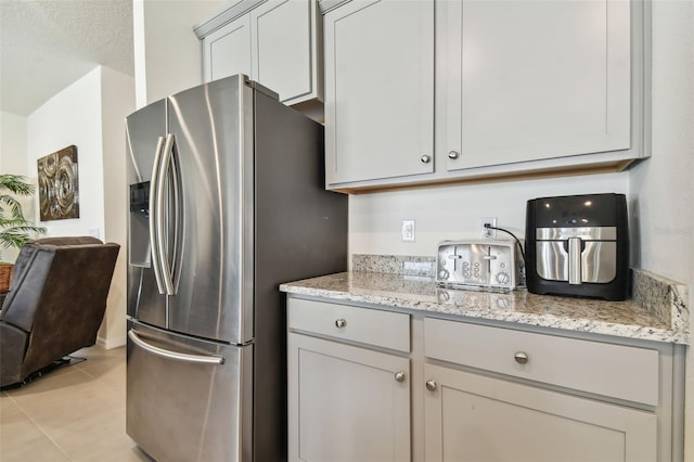 kitchen featuring gray cabinets, stainless steel fridge, light stone counters, and light tile patterned floors