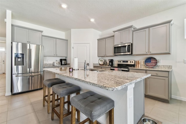 kitchen featuring sink, a kitchen bar, an island with sink, a textured ceiling, and stainless steel appliances