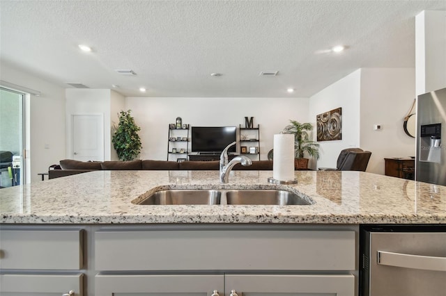 kitchen featuring light stone counters, sink, a textured ceiling, and a center island with sink