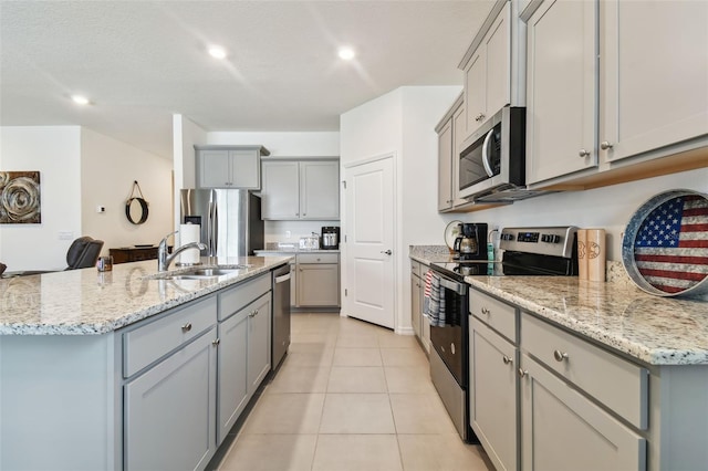 kitchen with sink, light tile patterned floors, appliances with stainless steel finishes, gray cabinetry, and a center island with sink