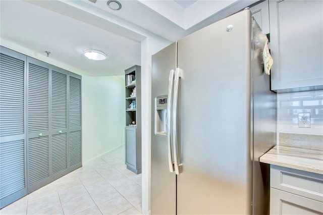 kitchen featuring fridge with ice dispenser, light tile patterned flooring, and light stone countertops