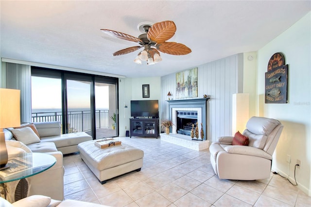 living area featuring a wall of windows, a brick fireplace, light tile patterned flooring, and ceiling fan