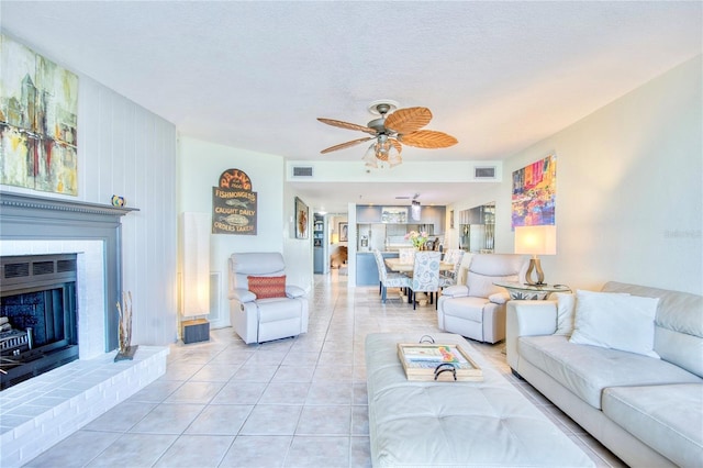 living area featuring light tile patterned floors, a fireplace, visible vents, and a ceiling fan