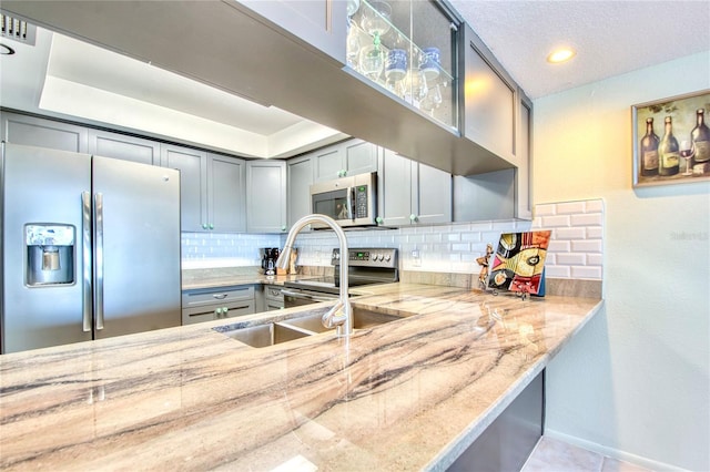 kitchen with light stone counters, tasteful backsplash, gray cabinetry, appliances with stainless steel finishes, and tile patterned floors