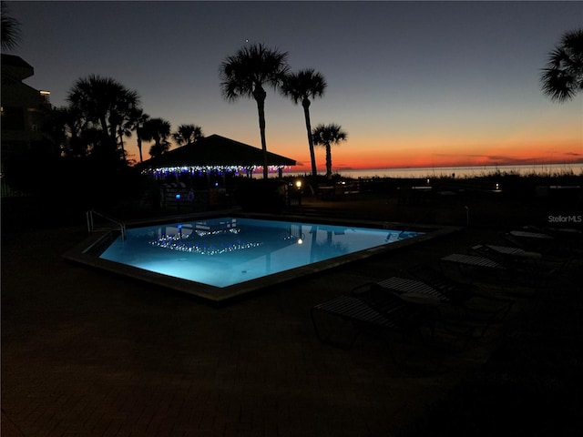 pool at dusk featuring a water view and a community pool