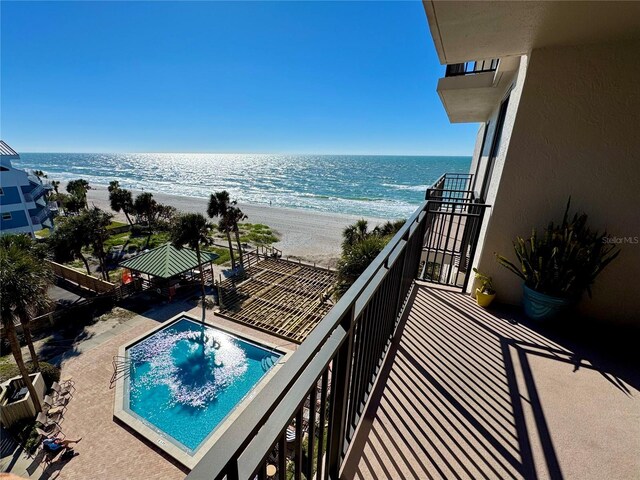 balcony with view of water and beach and view of pool area