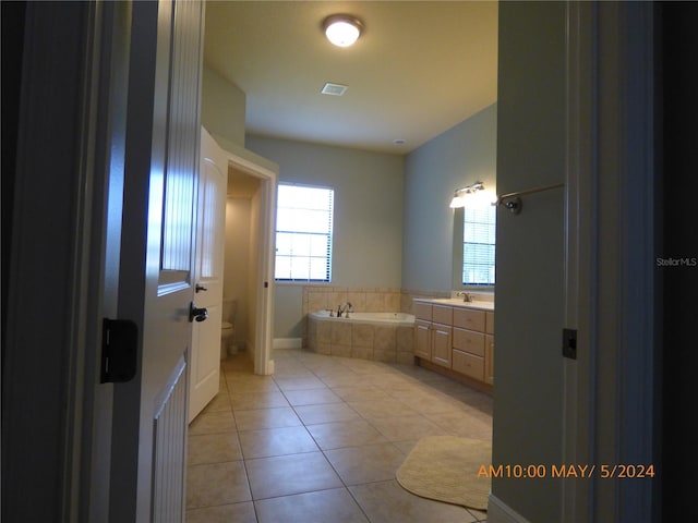 bathroom featuring toilet, tile patterned flooring, vanity, and tiled bath