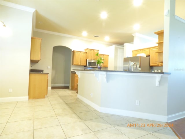 kitchen with appliances with stainless steel finishes, light tile patterned flooring, kitchen peninsula, ornamental molding, and a breakfast bar