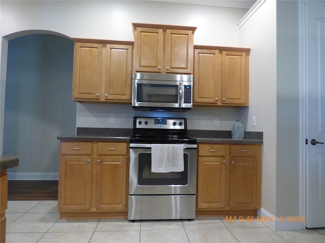 kitchen with stainless steel appliances, light tile patterned floors, and dark stone counters