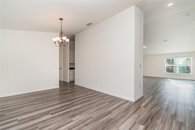 spare room featuring a notable chandelier, wood-type flooring, and vaulted ceiling