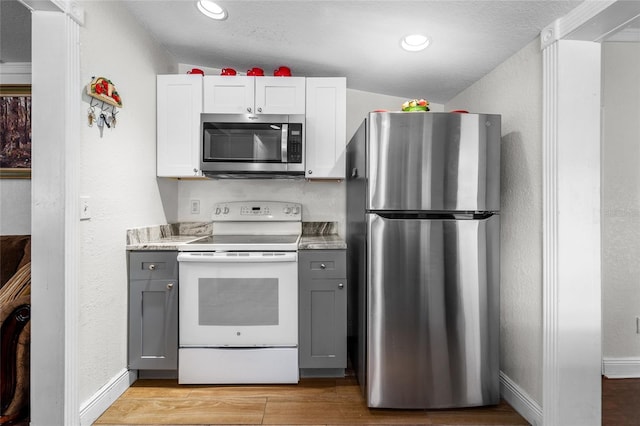 kitchen featuring white cabinetry, stainless steel appliances, lofted ceiling, gray cabinets, and light hardwood / wood-style flooring