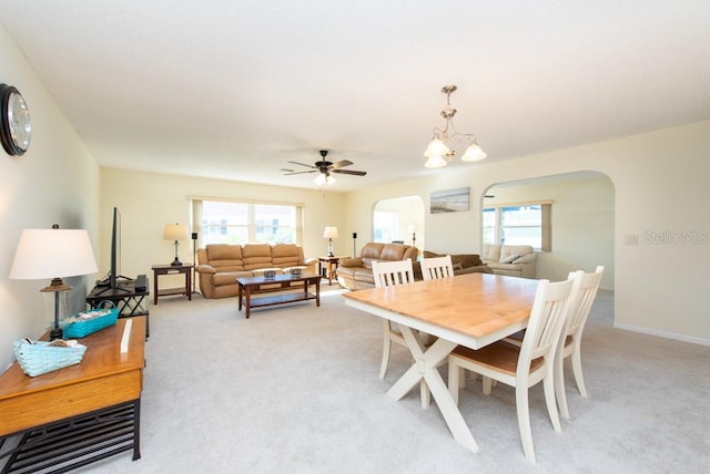 carpeted dining room featuring a healthy amount of sunlight and ceiling fan with notable chandelier