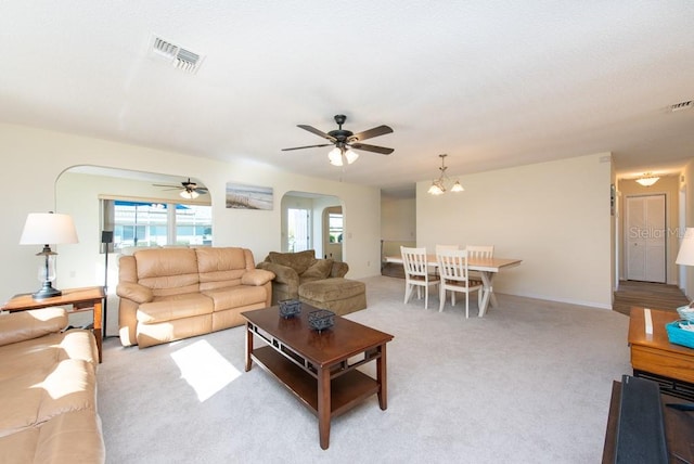 carpeted living room with ceiling fan with notable chandelier