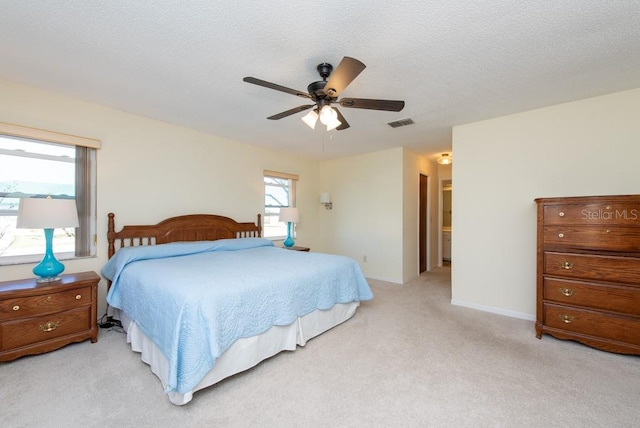 bedroom with light carpet, a textured ceiling, ensuite bath, and ceiling fan